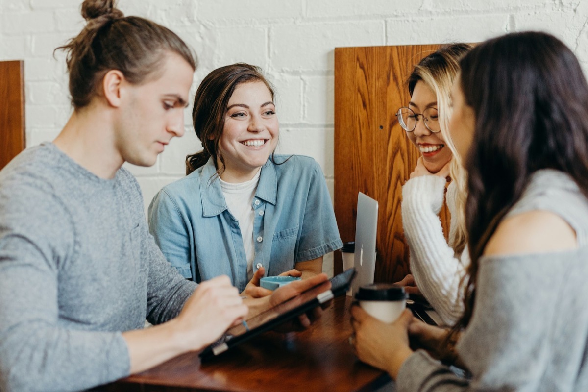 Vier collega's lachend rond een tablet aan tafel
